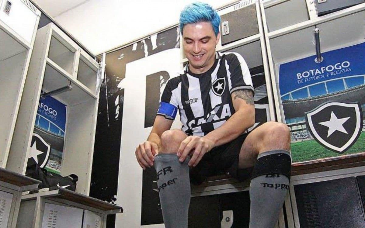 Felipe Neto com cabelo azul usando uniforme completo do Botafogo no vestiário do Estádio Nilton Santos